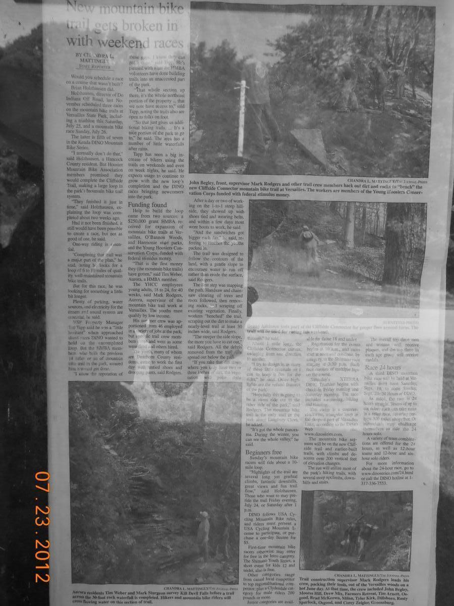 Black and white newspaper article discussing the development of a new mountain bike trail, featuring images of trail crew members working on the trail, along with text about the project's funding and community involvement. The article highlights contributions from local volunteers and mentions the use of federal stimulus money for the trail's completion. Versailles State Park mountain bike trail.