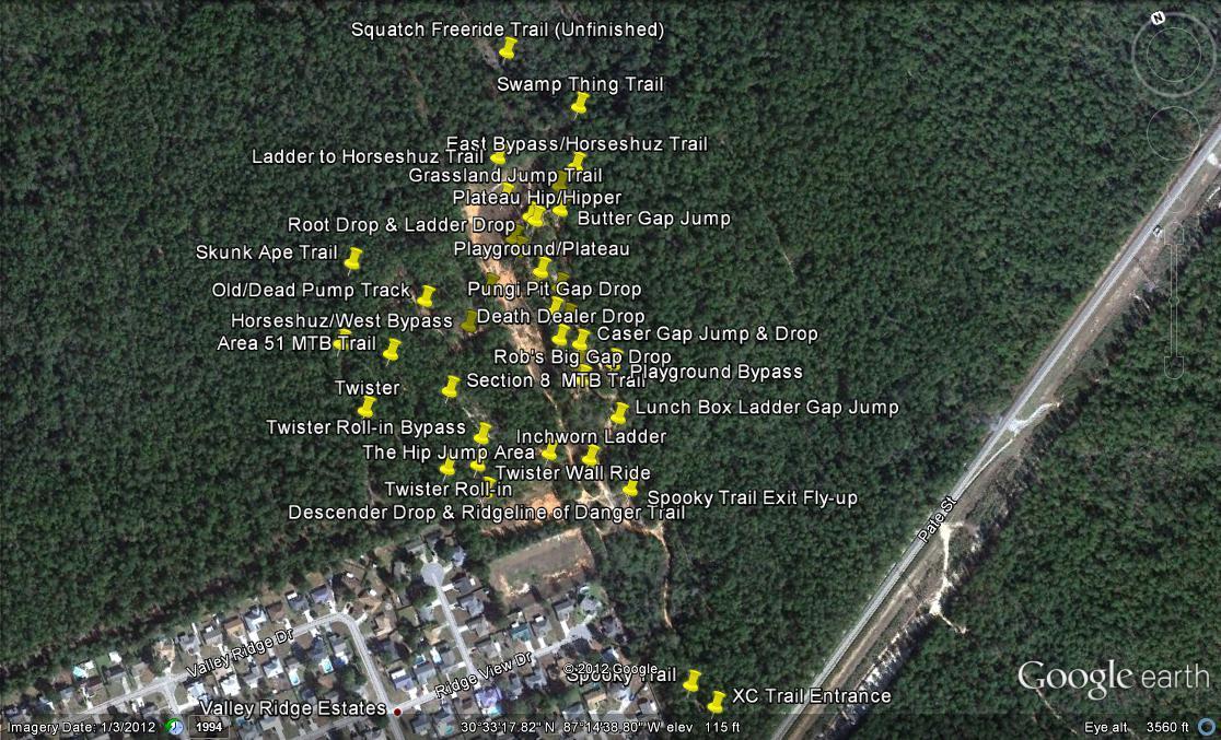Aerial view of a mountain biking trail system, featuring various trails and jumps labeled with yellow markers. The surrounding area includes dense forest and residential neighborhoods, with notable trails such as "Sasquatch Freeride Trail," "Death Dealer Drop," and "Butter Gap Jump." The image captures the layout of trails and features available for mountain biking. Games Loop mountain bike trail.