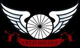 A logo featuring a stylized bicycle wheel with white wings on either side, set against a black background. Below the wheel is a red banner with the text "VELO SMART."