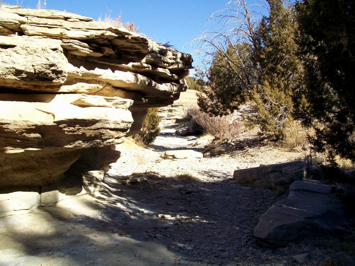 A rocky pathway surrounded by layered stone formations and sparse vegetation under a clear blue sky. South Shore Lake Pueblo mountain bike trail.