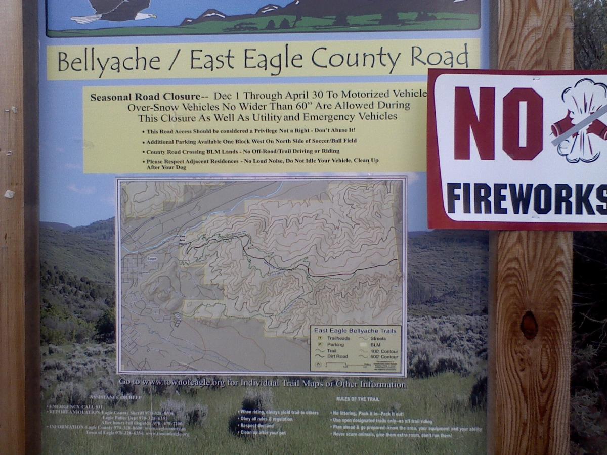 Signage detailing seasonal road closures for Bellyache/East Eagle County Road, featuring a map of local trails, regulations for over-snow vehicles, and reminders about noise and parking. A "No Fireworks" sign is prominently displayed alongside the informational content. The Boneyard mountain bike trail.