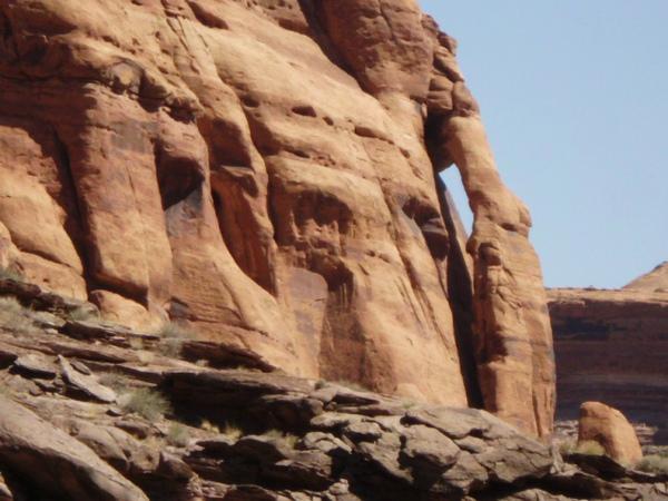 A close-up view of rugged, reddish-brown rock formations, showcasing the natural textures and patterns of the stone against a clear blue sky. The image highlights the geological features and layers of the landscape. Klondike Bluffs mountain bike trail.