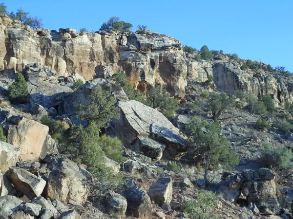 Rocky terrain with cliffs, scattered boulders, and sparse vegetation under a clear blue sky. Gunny Loop mountain bike trail.