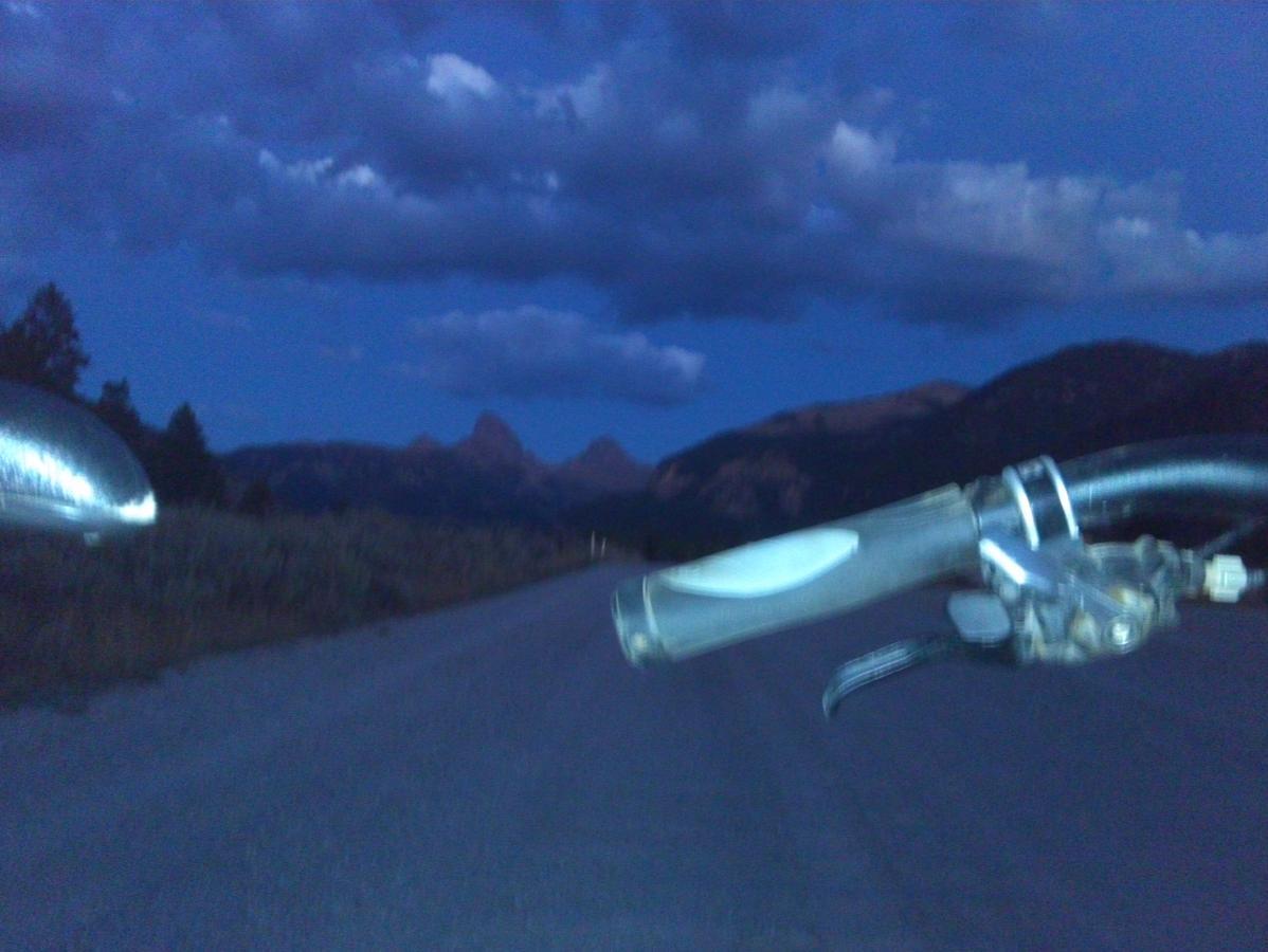 A view from the handlebars of a bicycle along a gravel road at twilight, with mountains and a cloudy sky in the background. Mill Creek mountain bike trail.