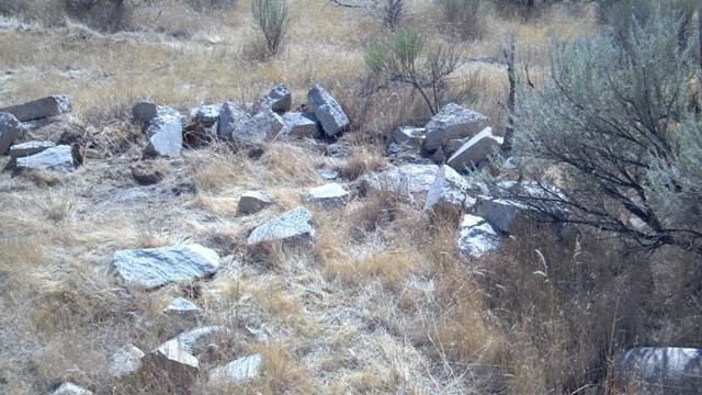 Rocky debris scattered across dry, grassy land with sparse vegetation and small shrubs in the background. Ada/Eagle Bike Park mountain bike trail.