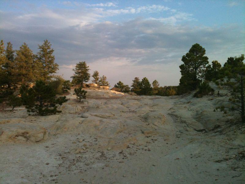 A rocky landscape with scattered trees under a partly cloudy sky, showcasing a natural setting with light-colored stone surfaces and a serene atmosphere. Ute Valley Park mountain bike trail.