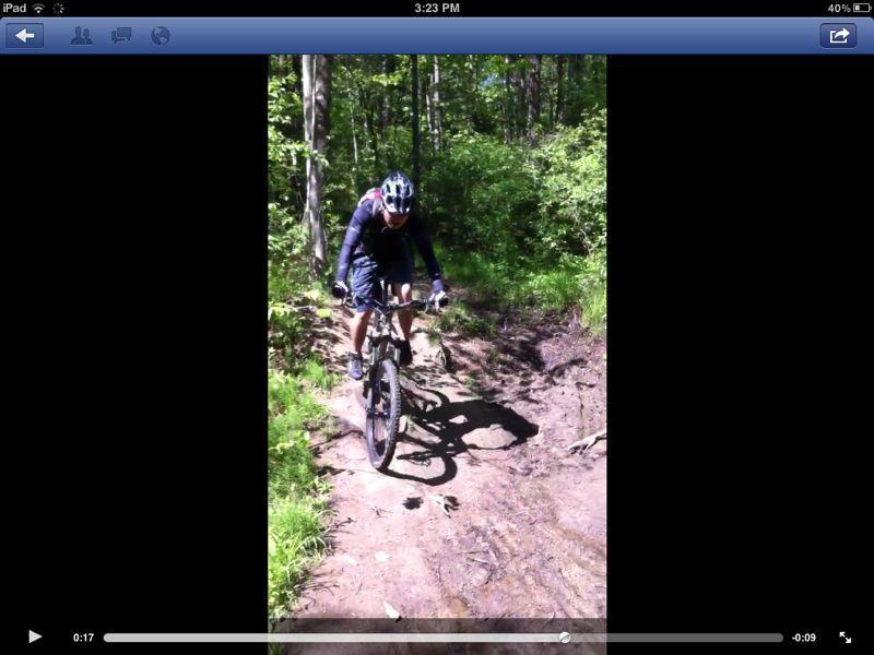 A person riding a mountain bike on a muddy trail surrounded by lush green trees. Cemetery Loop mountain bike trail.