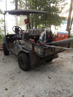 An off-road utility vehicle parked on a gravel path, with tools in the back, including a leaf blower and a cooler. The vehicle is partially shaded by surrounding trees. Paynes Creek mountain bike trail.