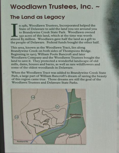 Image alt tag: A historical information sign detailing the legacy of Woodlawn Trustees, Inc. and their contribution to Brandywine Creek State Park in Delaware. The sign features text describing the organization’s efforts to preserve land, along with a map highlighting the Woodlawn Tract and surrounding areas. Brandywine State Park mountain bike trail.