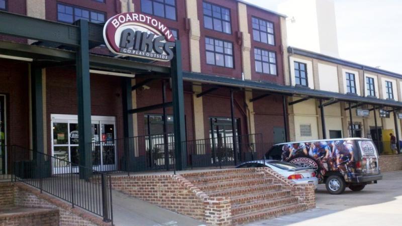 Exterior view of Boardtown Bikes, a bike shop located in a brick building with large windows. The entrance features a sign with the store