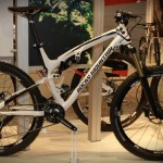 A sleek white and black mountain bike displayed in a showroom, featuring large tires and a modern design. The bike has a prominent brand name along the frame and is positioned alongside other bicycles in the background, highlighting its sporty and high-performance appearance.