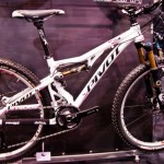A white Pivot mountain bike displayed at an exhibition, featuring a sleek frame design, large tires, and high-quality suspension components. The bike is showcased against a dark background, highlighting its modern aesthetics and attention to detail.