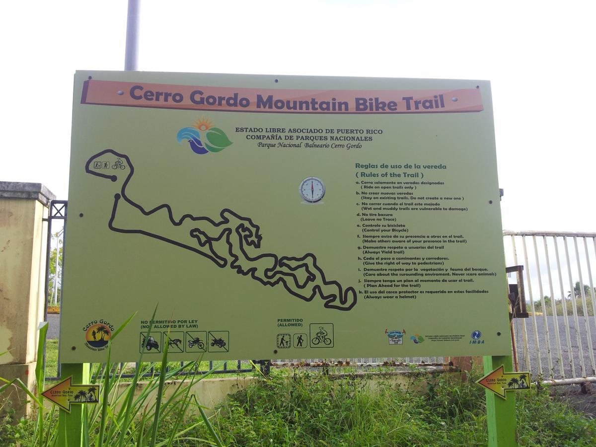 Sign for Cerro Gordo Mountain Bike Trail in Puerto Rico, featuring a trail map and rules for trail use, including guidelines for cyclists and hikers. The sign is prominently displayed with colorful graphics and text in both Spanish and English. Cerro Gordo Trail mountain bike trail.