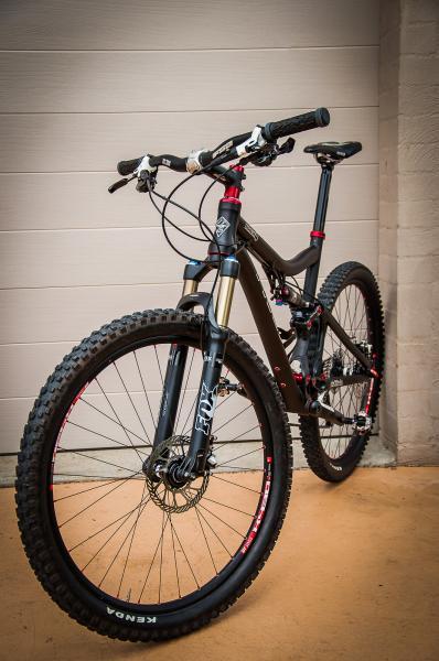 Pivot Mach 4: A black mountain bike with red accents, featuring a front suspension fork, wide tires, and a sleek design, leaning against a light-colored garage door.