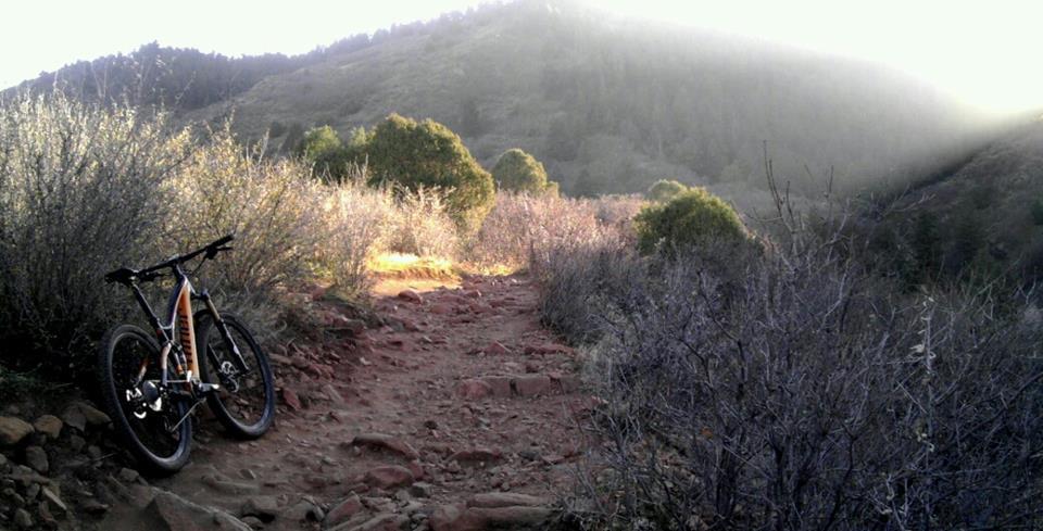 A mountain bike parked beside a rocky trail, surrounded by sparse vegetation and rolling hills under soft sunlight. The scene captures the essence of a natural landscape ideal for outdoor biking adventures. Deer Creek Canyon mountain bike trail.