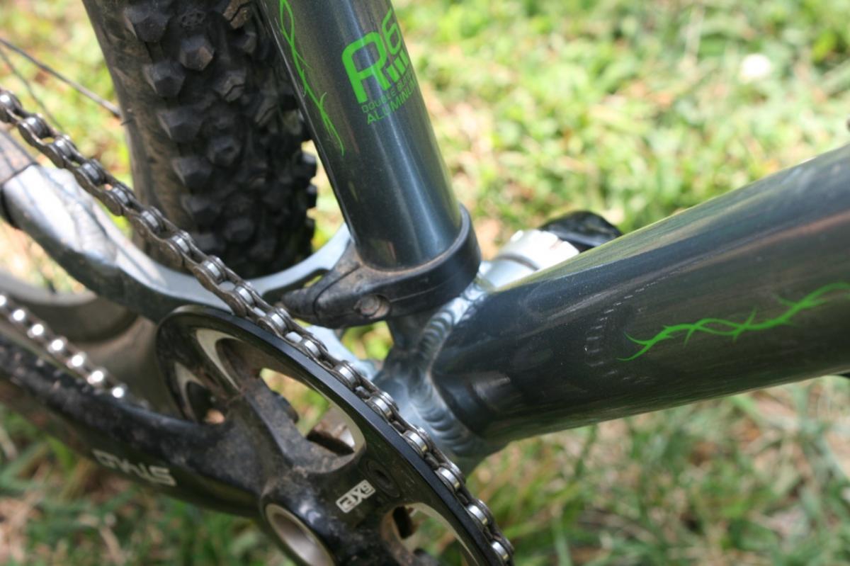 Redline D660 29er: Close-up view of a mountain bike's drivetrain and bottom bracket area, featuring a gray frame with green graphics, a chainring, and a chain against a background of grass.