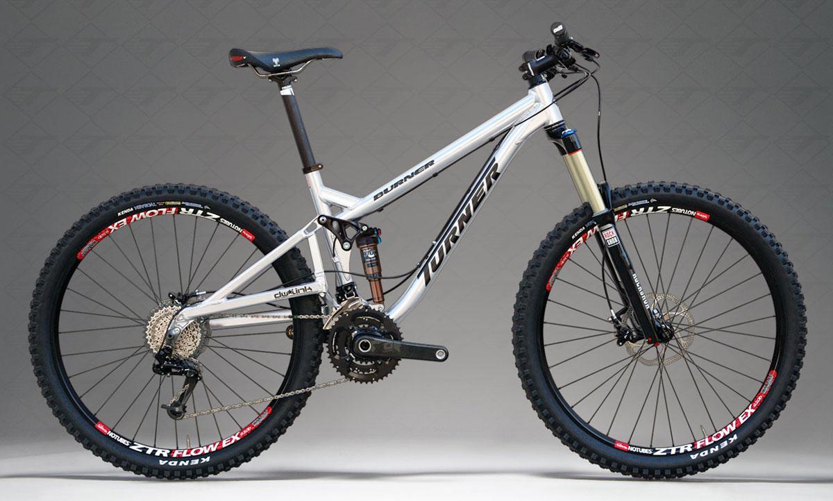 Turner Burner: Image of a Turner mountain bike featuring a silver frame, equipped with dual suspension, wide knobby tires, and disc brakes. The bike showcases a modern design suitable for off-road cycling, with visible gear components and a sleek appearance against a neutral background.