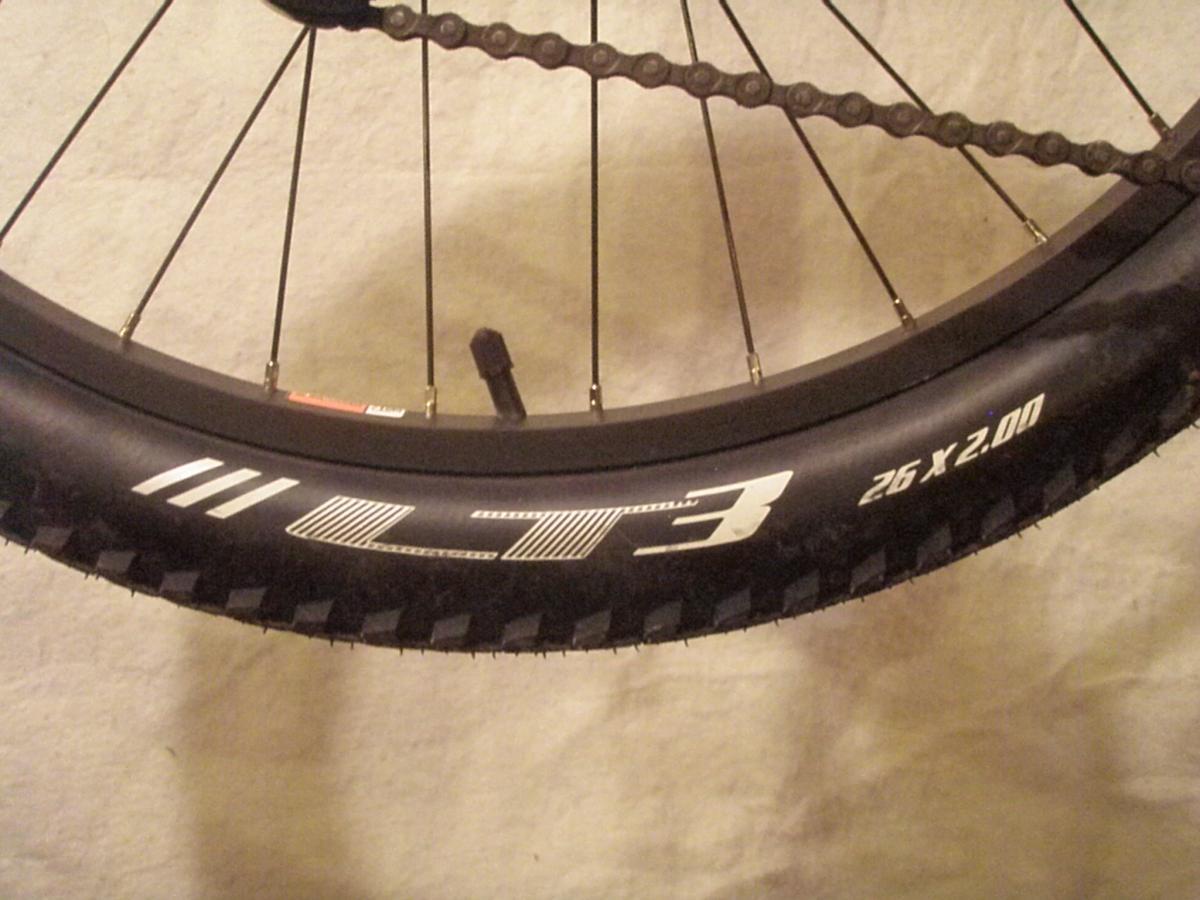 Bontrager LT3: Close-up image of a bicycle tire, displaying the tread pattern and sidewall markings. The tire is labeled "LT3" and has dimensions of "26 x 2.00". The background is neutral, providing contrast to the tire.