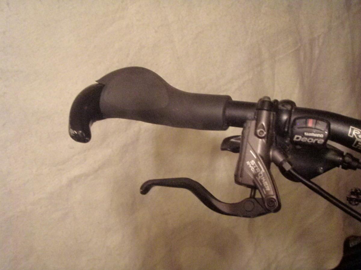 Ergon GC2: Close-up of a bicycle handlebar featuring a textured black grip and a Shimano Deore brake lever, with part of a gear shifter visible on the side.