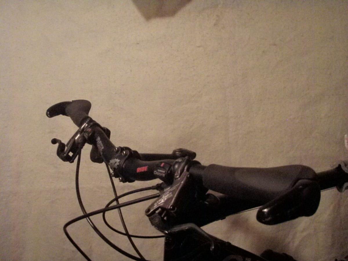 Ergon GC2: A close-up view of a bicycle handlebar set against a plain, light-colored wall. The handlebar includes grips, brake levers, and shift mechanisms, showcasing a well-used cycling component.