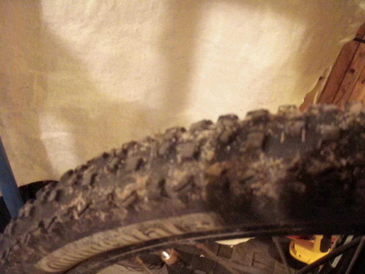 Continental Mountain King II: Close-up view of a bicycle tire showing worn tread and dirt accumulation, with a blurred background of a wall and tools.