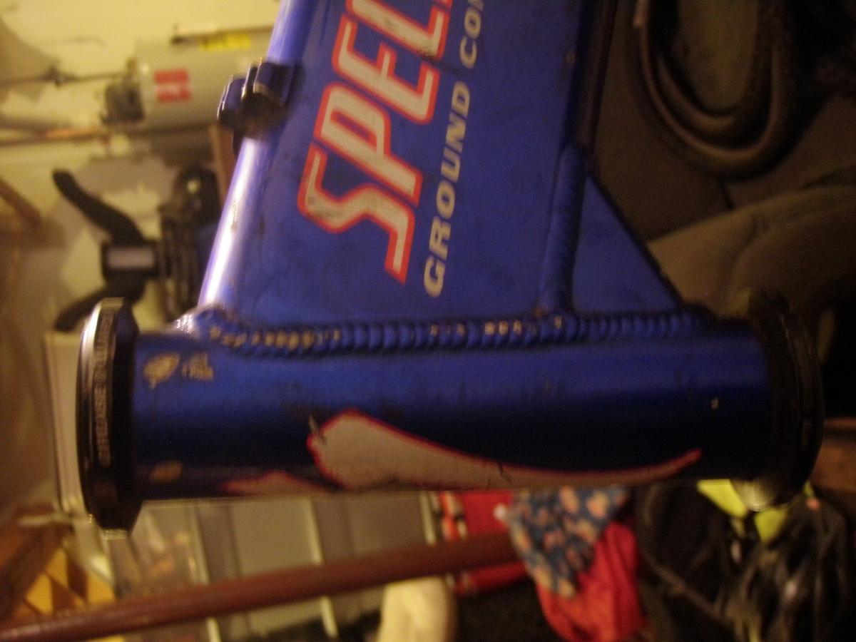 Specialized FSR: An image of a blue bicycle frame showing visible wear and tear, with a prominent logo that reads "SPECIALIZED GROUND CONTROL." The frame is viewed from the side, highlighting scratches and paint scuffs. In the background, various blurred items suggest a garage setting.