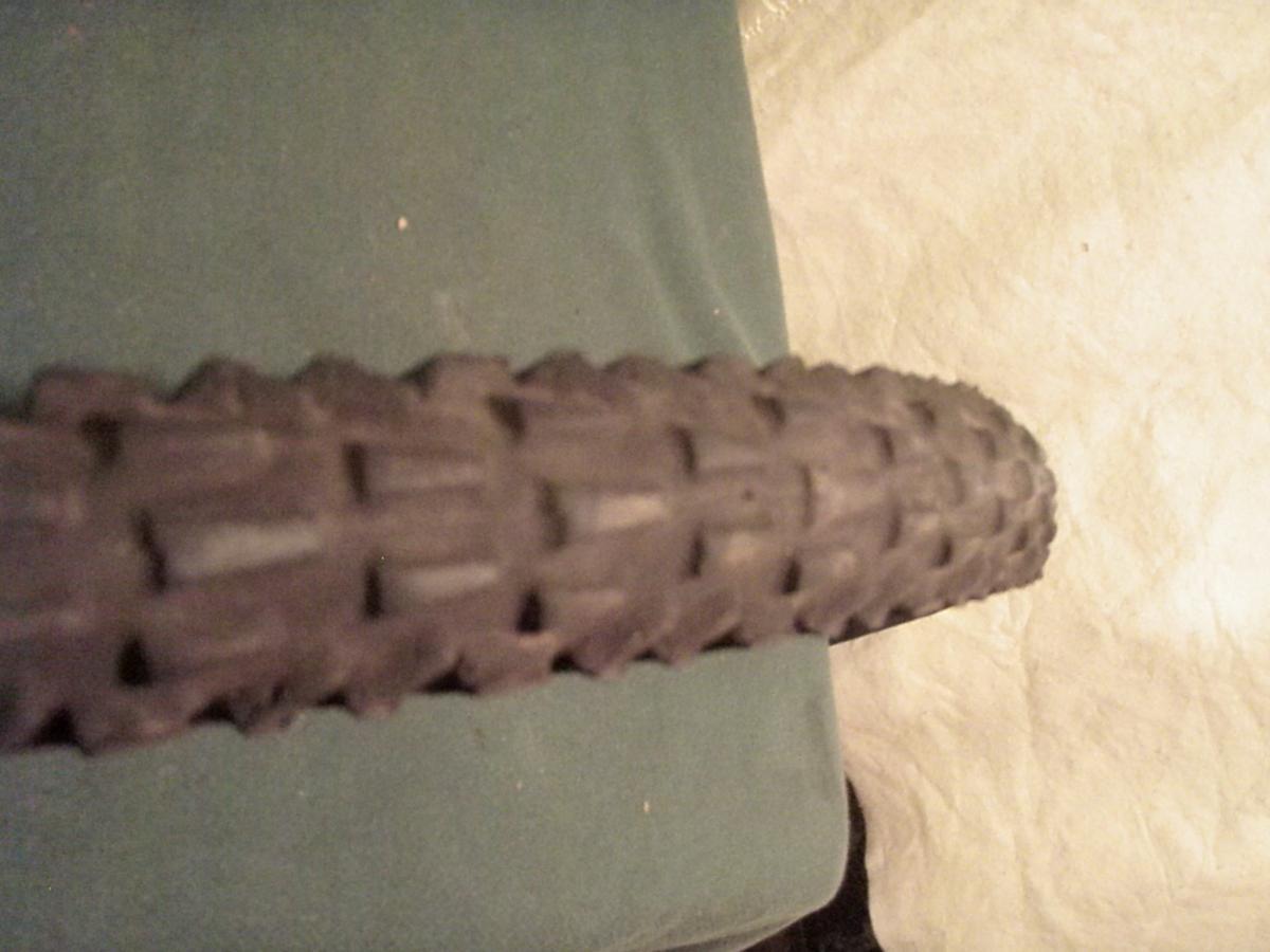 Panaracer Dart: Close-up view of a textured bicycle tire resting on a green surface, highlighting the tread pattern.