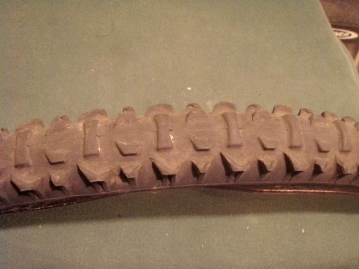 Panaracer Smoke: Close-up image of a mountain bike tire showing its tread pattern, designed for traction on rough terrain. The tire is positioned horizontally against a green background.