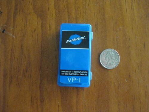 Park VP-1 Vulcanizing Patch Kit: A small blue container labeled "VP-1" from Patch Tool, used for bike tire puncture repair, placed next to a quarter for size reference. The container features a black logo and text indicating its use for patching tires.