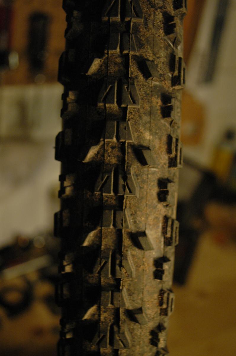 Maxxis Ardent: Close-up image of a worn bicycle tire showcasing the tread pattern and dirt accumulation. The background is blurred, providing focus on the tire's surface and textures.