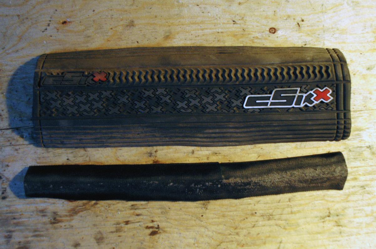 cSixx Chainstay Protector: Close-up of a black rubber bicycle tire patch kit on a wooden surface. The patch kit is labeled "csi x" and consists of a rectangular piece with a textured surface and a smaller cylindrical piece below it.