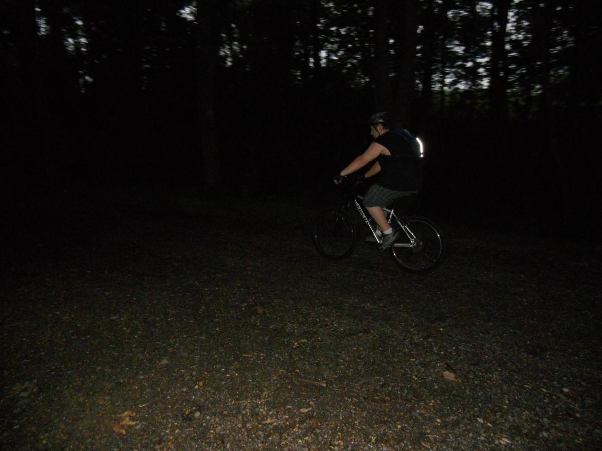 Trek 4500: A cyclist riding a mountain bike along a gravel path in a dark wooded area, wearing a helmet and reflective gear. The scene captures the essence of nighttime outdoor biking.