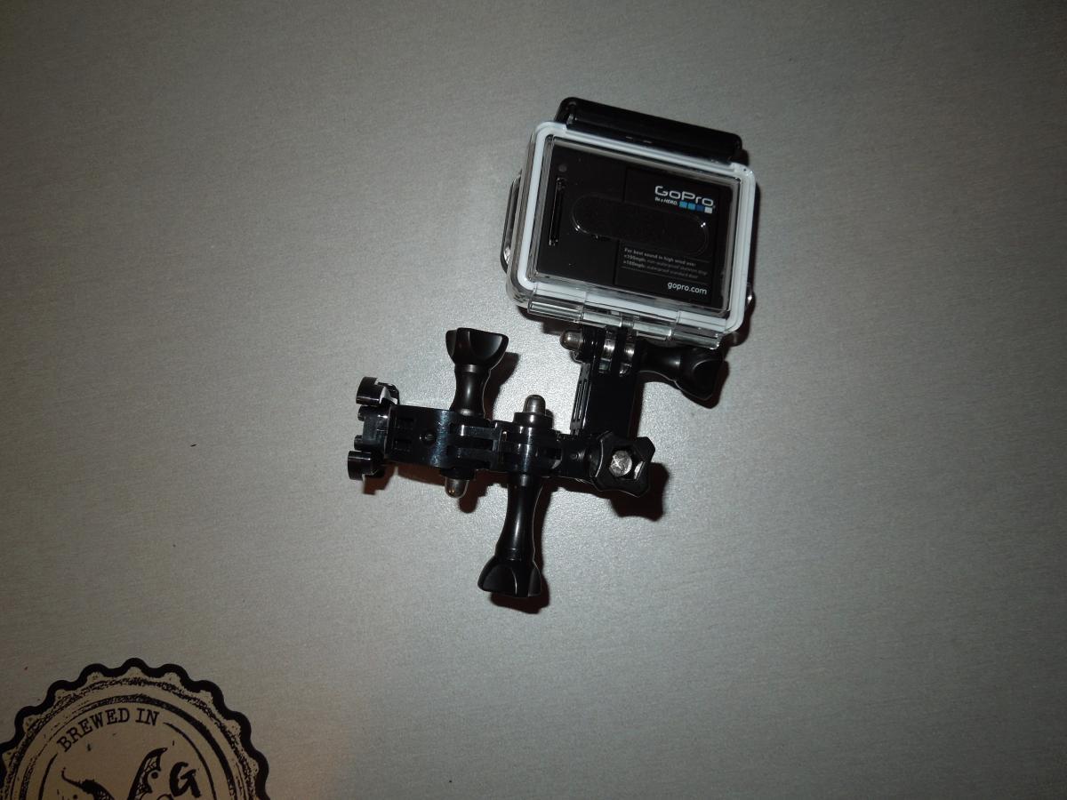GoPro Helmet Front Mount: A GoPro camera mounted on a flexible black tripod, positioned on a gray surface. The camera is encased in a transparent waterproof housing, showcasing its compact design and features.