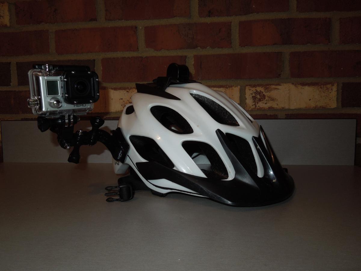 GoPro Helmet Front Mount: A white and black bicycle helmet mounted with a GoPro camera on the side, positioned on a flat surface against a brick wall.