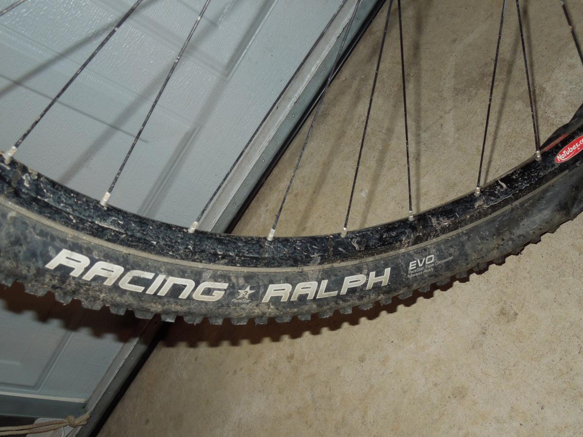 Schwalbe Racing Ralph: Close-up view of a mountain bike tire labeled "Racing Ralph" on a dirty rim, resting on a concrete surface with a garage door in the background.