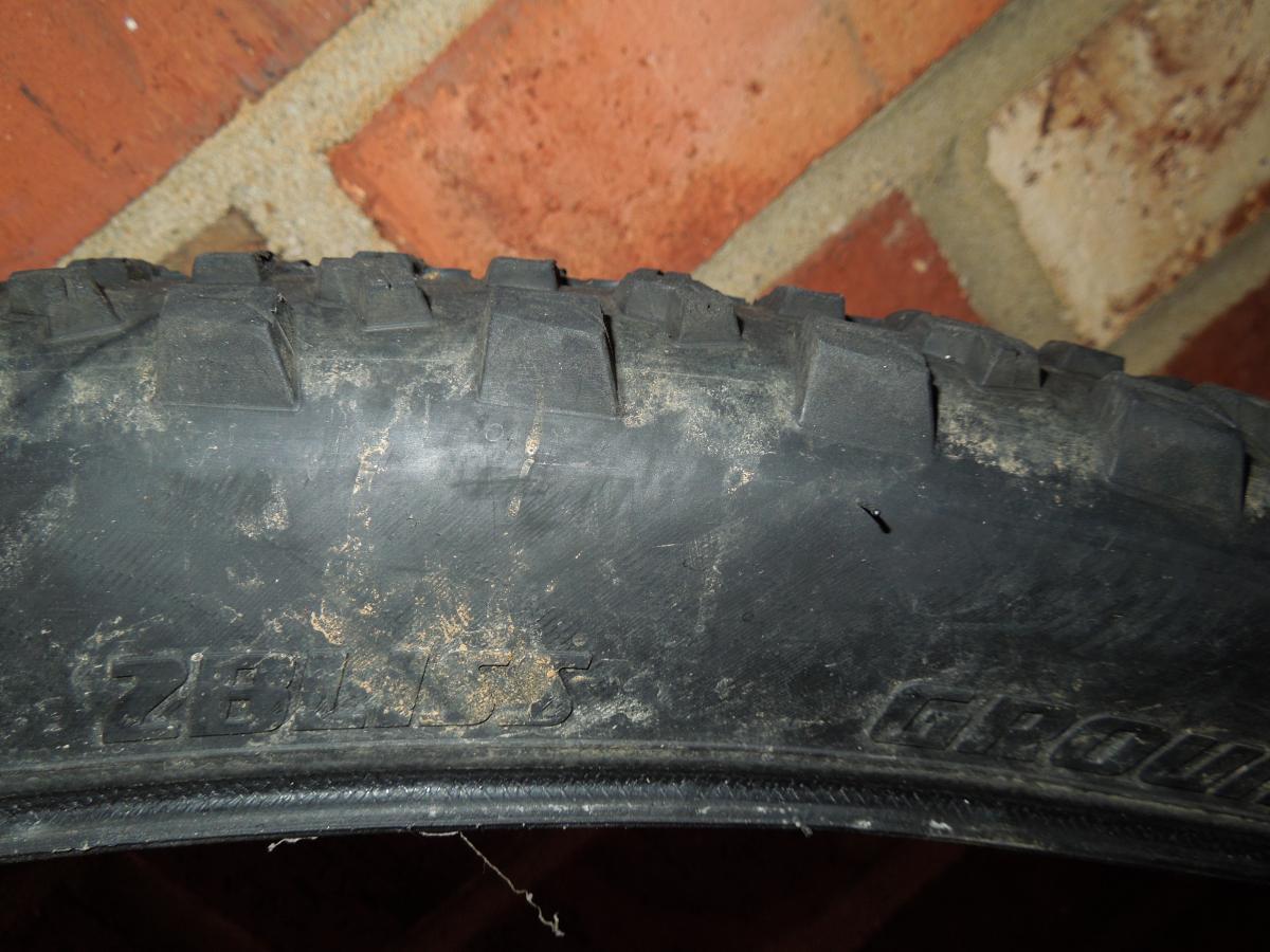 Specialized Ground Control: Close-up image of a worn bicycle tire, showing the tread pattern and some dirt on its surface, set against a background of brick.