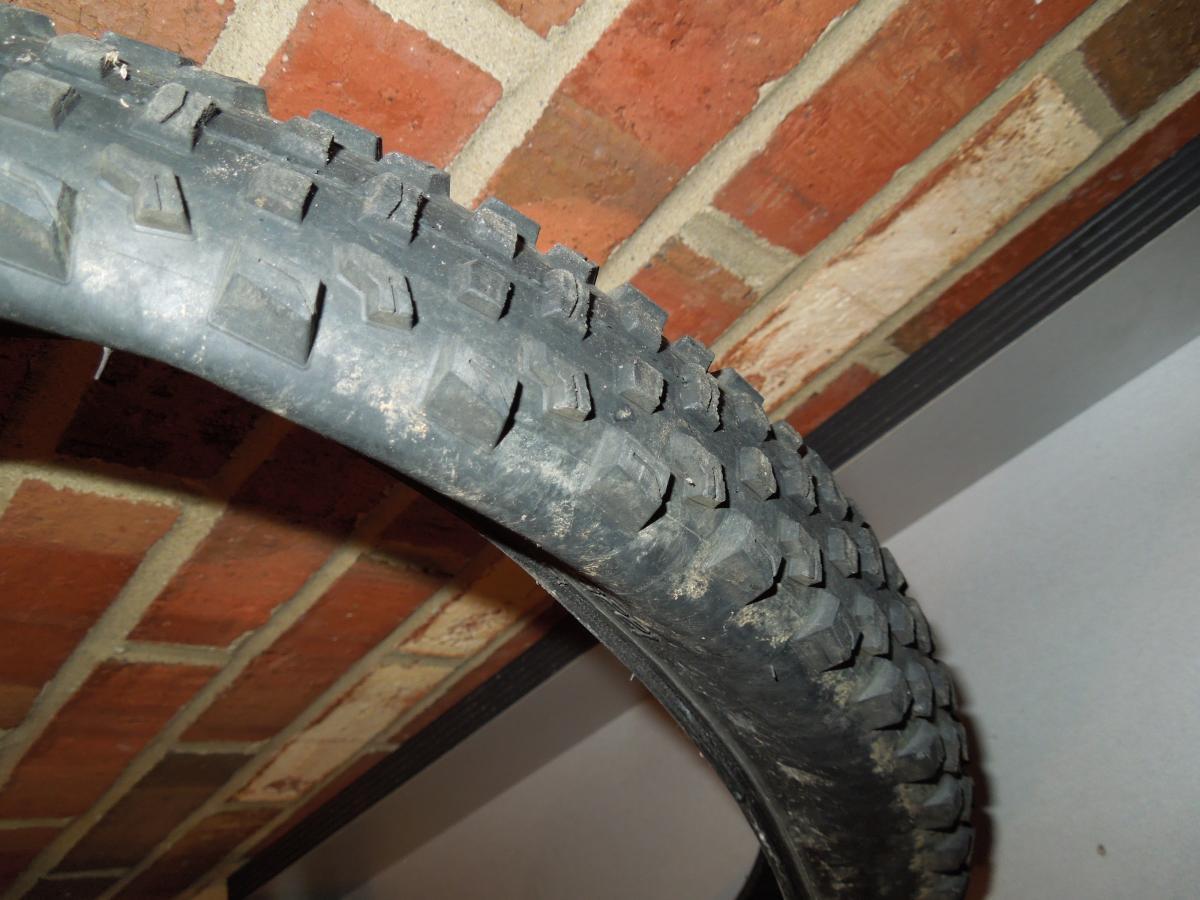 Specialized Ground Control: A close-up image of a bicycle tire with a textured tread pattern, partially leaning against a brick wall. The tire appears to have some dirt on it, indicating prior use. The background features a mix of red and beige bricks.