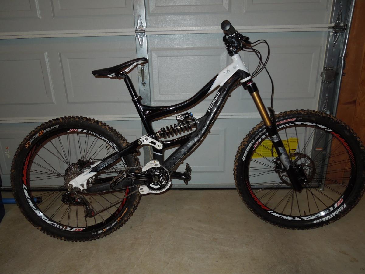 Continental Mountain King Race Sport: A black and white mountain bike with a full suspension system, featuring knobby tires and a detailed drivetrain, positioned against a garage backdrop. The bike showcases a sleek design and is equipped with disc brakes, highlighting its suitability for off-road riding.