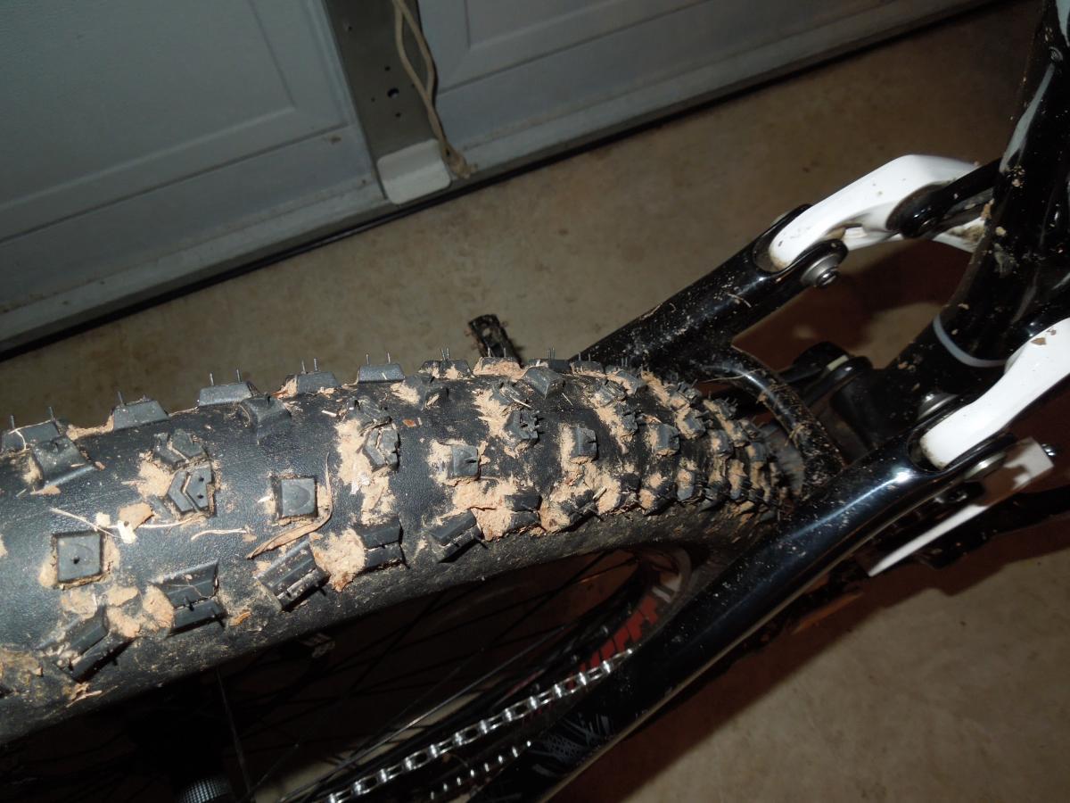 Continental Mountain King Race Sport: Close-up view of a muddy mountain bike tire, showing its tread pattern and some dirt clinging to the surface, with parts of the bike frame in the background.