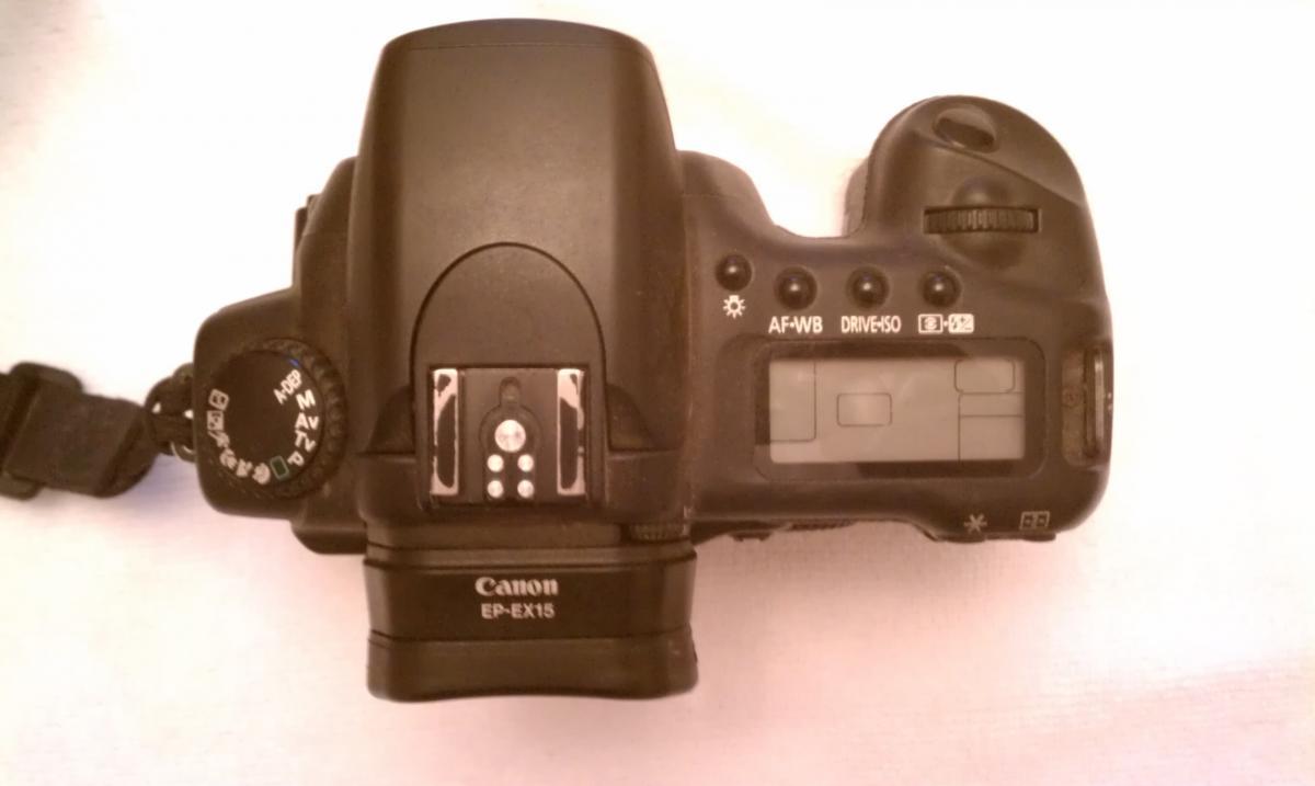 Canon 20D: Top-down view of a Canon DSLR camera, showing the camera body, control dials, and buttons, with a strap attached. The display screen and various settings indicators are visible.