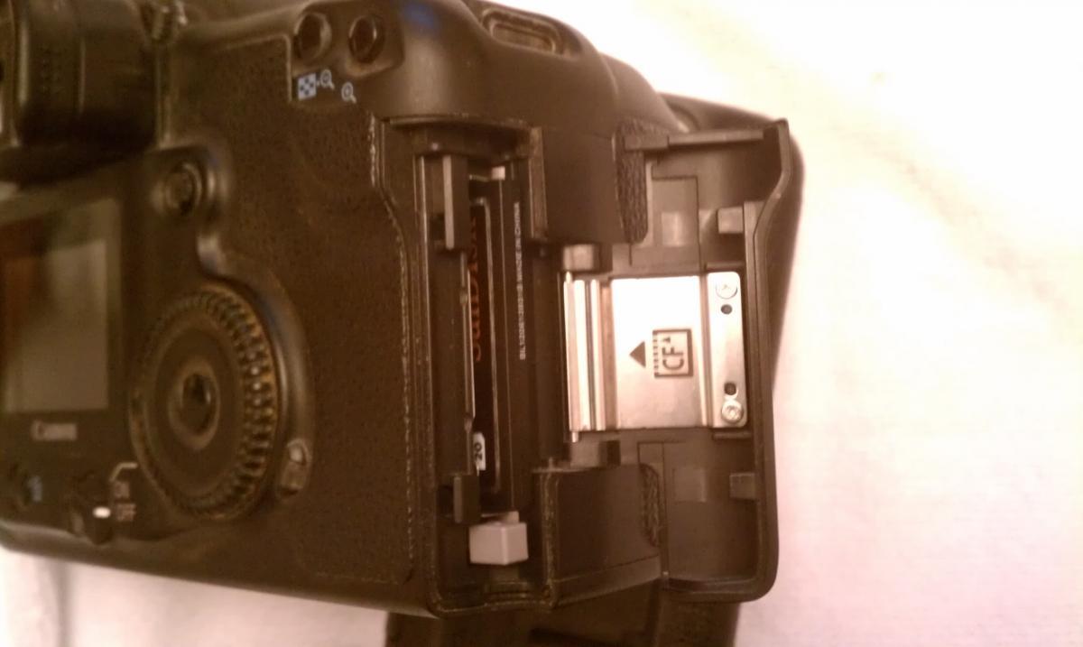 Canon 20D: Close-up view of the side compartment of a digital camera, showing an open slot for a memory card, indicating a CompactFlash card inserted. The camera body is black with various buttons and dials visible.
