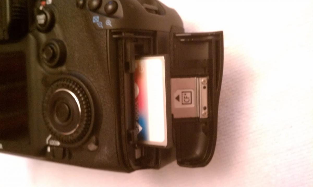 Canon 7D: Close-up view of a digital camera showing the memory card compartment with a memory card partially inserted and some controls visible on the camera body.