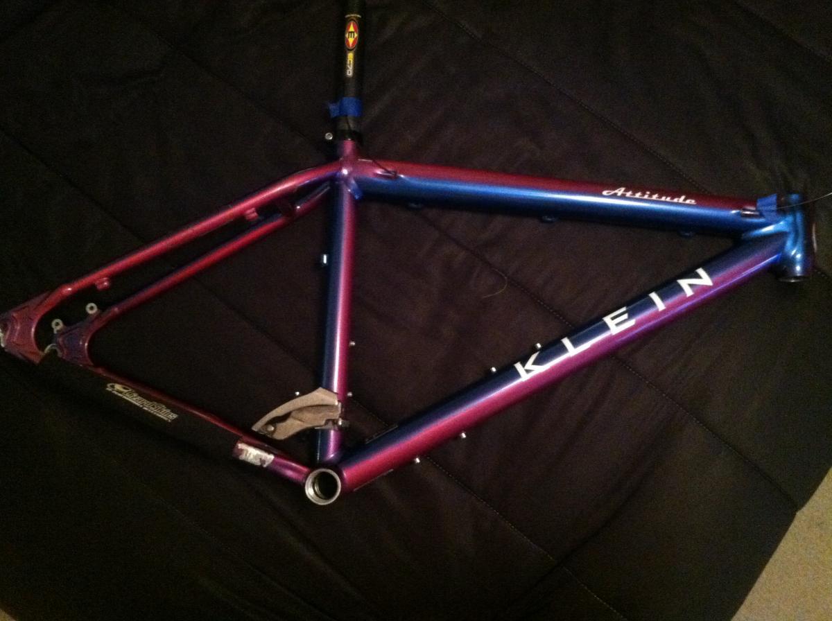 Klein Klein Attitude XX: Alt text: A purple and blue Klein bicycle frame lying flat on a dark surface. The frame features the brand name "Klein" prominently displayed, along with the word "Attitude" on the top tube. The frame has visible mounts for components and a shiny, gradient finish.