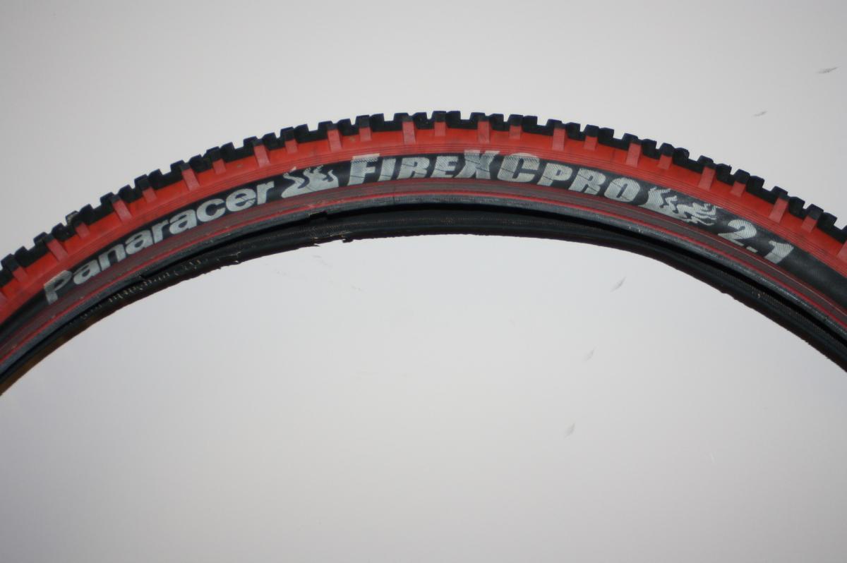 Panaracer Fire XC Pro: A close-up image of a Panaracer Fire XC Pro 2.1 mountain bike tire, showcasing the tread pattern and branding. The tire features a bold black and red design, highlighting its rugged texture suitable for off-road use.