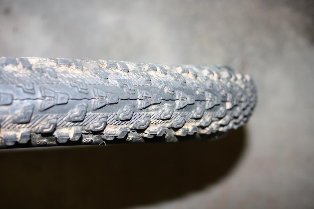 Bontrager Jones XR: Close-up of a bicycle tire showing its tread pattern, which is worn and dirtied, resting on a concrete surface.