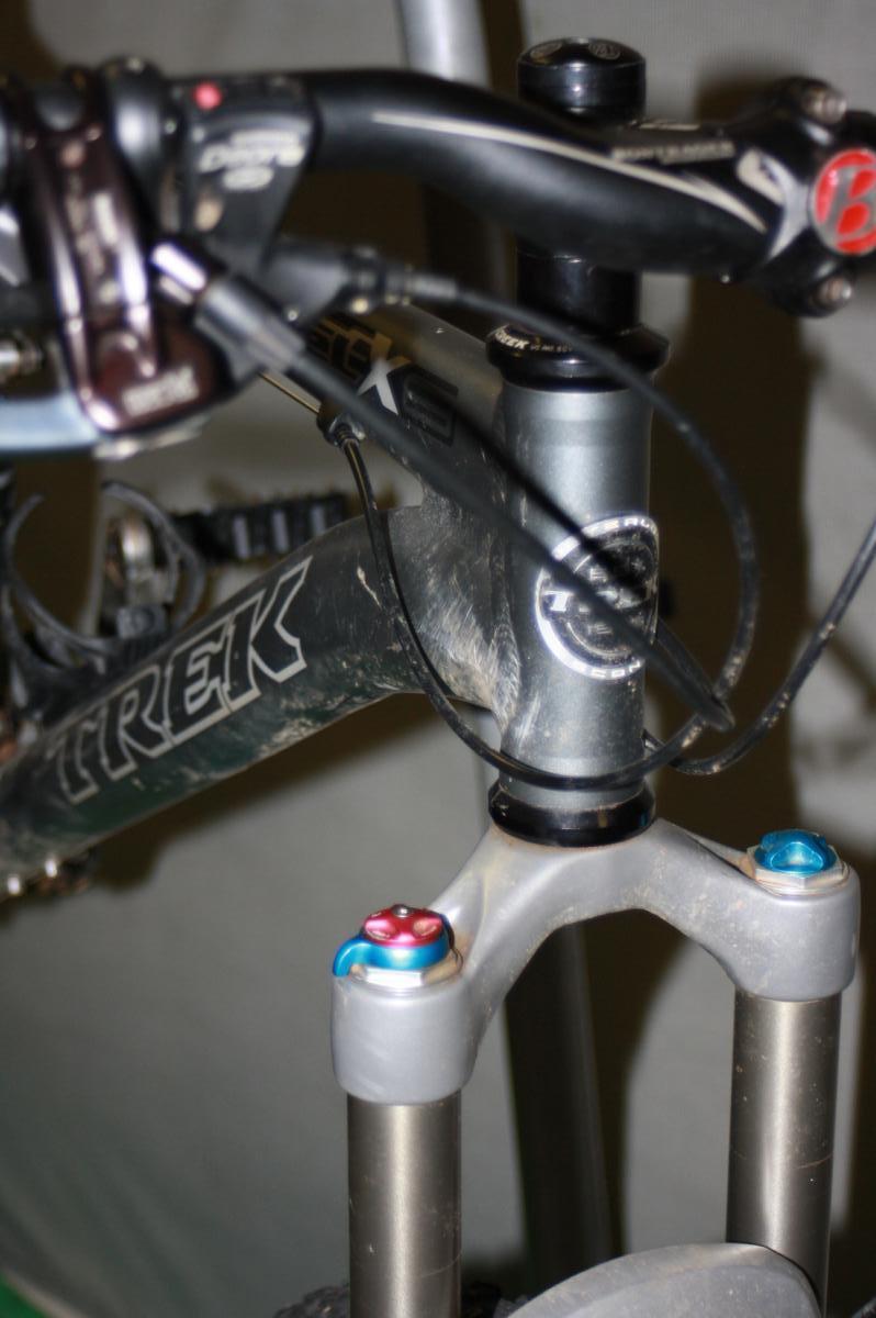 Trek Fuel EX 8: Close-up view of a mountain bike's handlebars and fork, showcasing the Trek logo on the frame, components of the steering mechanism, and colorful adjustment knobs on the fork. The image captures details of the bike's setup and condition.