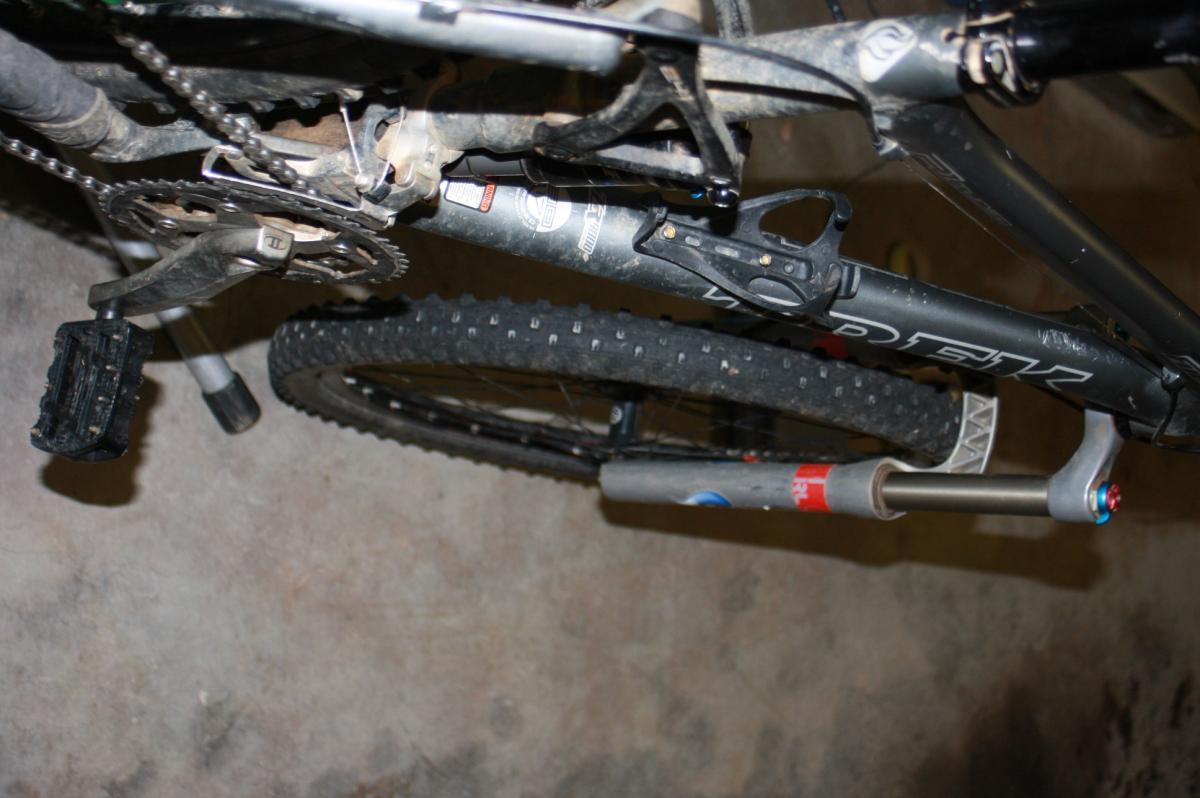 Trek Fuel EX 8: Alt text: Close-up view of a mountain bike's frame, pedals, and chain, resting upside down on a concrete surface. The bike shows signs of use with dirt and wear on its components.