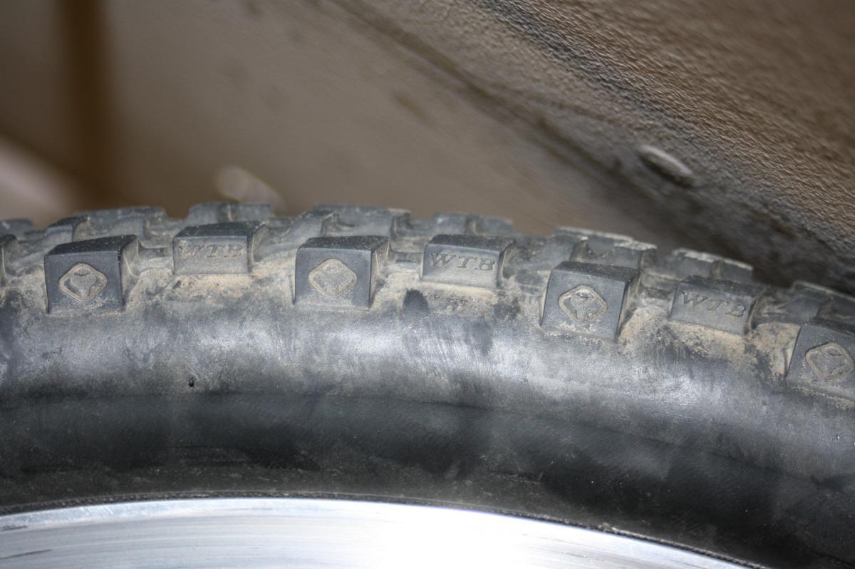 WTB Mutano Raptor: Close-up image of a rugged bicycle tire with visible tread patterns and dirt, featuring markings that read "WTB" and "WT8." The tire is mounted on a shiny metal rim.