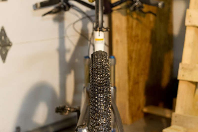 Kenda Small Block Eight: Close-up view of a mountain bike's rear tire, featuring a textured tread pattern, situated in a garage setting with wooden planks in the background.