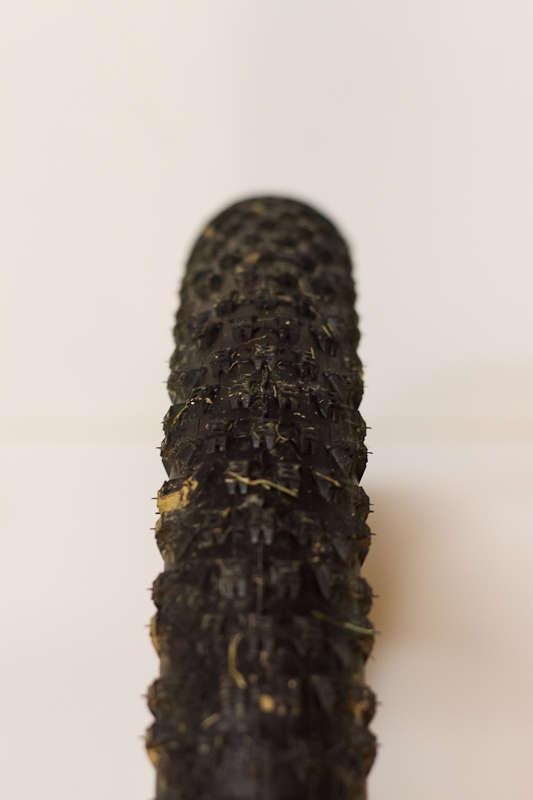 Kenda Slant Six: Close-up of a black bicycle tire resting on a white background, showcasing its textured tread pattern and slight debris embedded in the rubber.